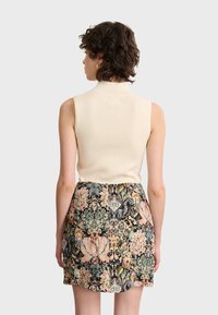 Top ribeteado sin mangas en color crema combinado con una falda corta estampada que presenta diseños florales y abstractos en tonos pasteles y oscuros.