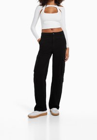 Bílý crop top s dlouhým rukávem, bočními výřezy a čtvercovým výstřihem, doplněný černými cargo kalhotami s bočními kapsami a volným střihem.