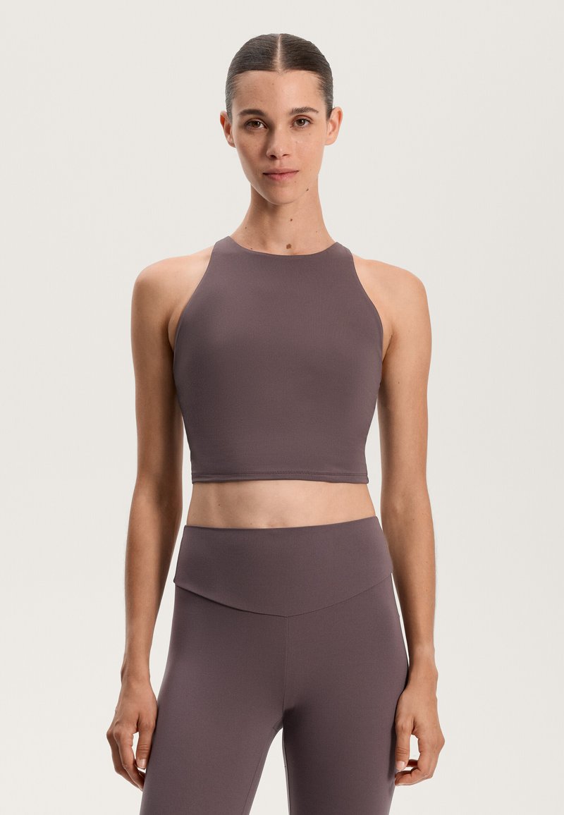 Hnedý športový crop top s vysokým výstrihom a dizajnom racerback, vyrobený z hladkej, elastickej tkaniny. Spárovaný s vyhovujúcimi legínami s vysokým pásom.