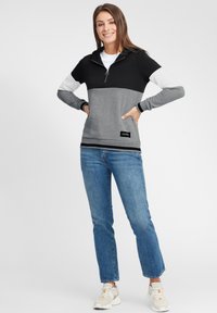 Pullover hoodie i svart, grått och vitt med en fjärdedels dragkedja. Har en mjuk textur och kontrasterande ribbade manschetter. Tillsammans med blå jeans.