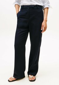 Marineblaue weite Hosen aus glattem Stoff, mit Fronttaschen und taillierter Passform. Kombiniert mit einfachen Flip-Flops.
