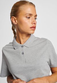 Graues Polohemd mit kurzen Ärmeln, Kragen und zwei grauen Knöpfen. Weicher Stoff, minimalistisches Design, geeignet für die Freizeit.