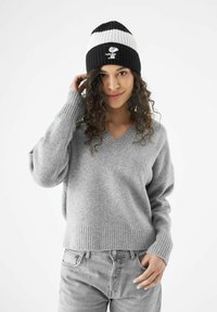 Grijze gebreide trui met een V-hals, geribbelde manchetten, gedragen met lichtgrijze jeans. Zwart-witte gestreepte beanie met een karakterlogo op de voorkant.