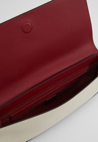 Åben hvid læder clutch-taske med dyb rød indvendig foring og indre lomme med stikninger.