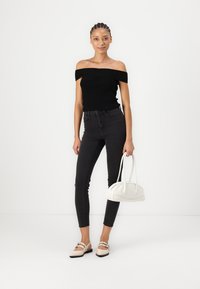 Juoda off-the-shoulder palaidinė, juodos aukšto juosmens džinsai, balta rankinė ir smėlio spalvos butai su dirželiais. Lygi tekstūra ir prigludęs dizainas.