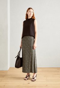 Top sin mangas negro combinado con una falda larga de estampado. La modelo sostiene una bolsa de mano negra y lleva sandalias negras con tiras. Suelo de madera clara.