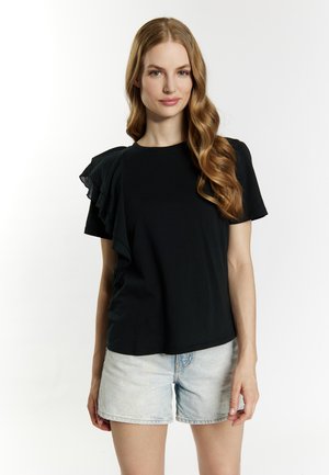 Zwarte t-shirt met korte mouwen en een gerimpelde accent op één schouder. De stof lijkt zacht met een gladde textuur. Gecombineerd met lichte spijkerbroekshorts.
