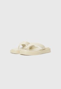 Infradito beige chiaro con suola piatta, caratterizzati da una fascia larga e design a giunzione. Realizzati in materiale flessibile con una texture liscia.