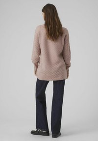 Long-sleeve, light pink knit sweater with a chevron pattern, paired with dark blue wide-leg jeans and black loafers.