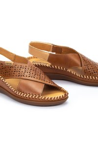 Sandalias de cuero marrón con patrones florales troquelados, detalles de costura y plantilla acolchada. Diseño de parte trasera abierta para facilitar su uso.
