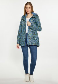 Vandeniui atsparus mėlynas lietpaltis su žaliu leopardų raštu, su reguliuojamu gobtuvu, užtrauktuku priekyje ir dviem šoninėmis kišenėmis; derinamas su mėlynomis džinsinėmis kelnėmis ir baltomis sportbačiais.