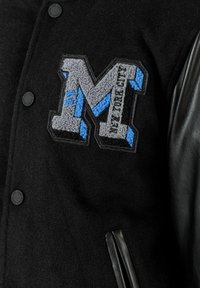 Giacca varsity in lana nera con maniche in pelle, caratterizzata da una grande lettera "M" ricamata in grigio e blu e bottoni a pressione neri.