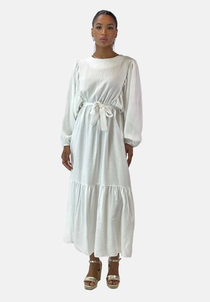 Robe blanche à manches longues avec taille froncée et ceinture à nouer. Le tissu a un aspect légèrement texturé et s'évasent vers un ourlet à volants.