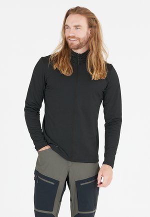 Sort zip-up langærmet top lavet af letvægts, tekstureret stof; parret med grønne og mørkeblå bukser med flere lommer.