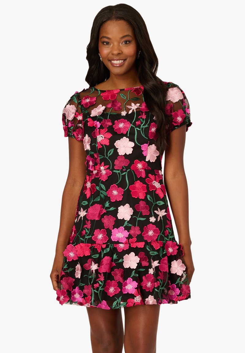 Černé šaty s krátkými nafouknutými rukávy, zdobené barevným květinovým vyšíváním v růžové a zelené barvě. Volánkový lem přidává designu objem.