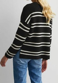 Schwarzer Strickpullover mit weißen horizontalen Streifen, getragen von einer Person mit langen blonden Haaren und blauen Jeans, von hinten und von der Seite gezeigt.