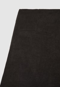 Dunkelbrauner gerippter Stoff mit einer kleinen horizontalen Gesäßtasche an einem Kleidungsstück, wahrscheinlich einer Hose oder einem Rock.