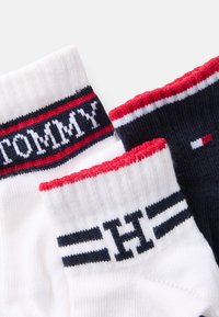 Pamuk čarape u bijeloj i mornarskoj plavoj boji, s crvenim i bijelim prugastim manžetama. Gornja bijela čarapa ima izvezenu riječ "TOMMY"; mornarska čarapa ima detalj s logotipom.