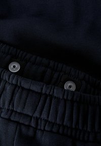 Acercamiento de cinturas elásticas en azul marino oscuro con dos botones transparentes cosidos a correas ajustables negras dentro de la tela.