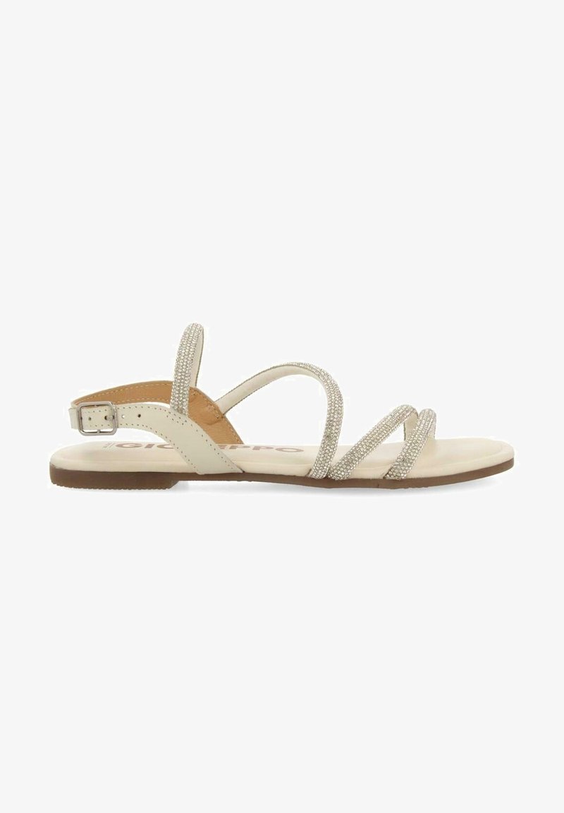 Sandale plate beige avec des fines lanières scintillantes et une boucle ajustable à la cheville sur une semelle marron, vue de côté sur fond blanc.