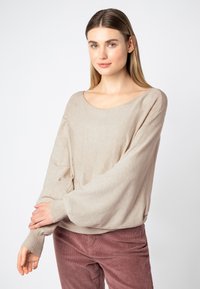 Licht beige gebreide trui met een brede ronde halslijn en lange, losse mouwen. Draag het met zachte, roze corduroybroeken die een ontspannen pasvorm hebben.