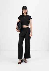 Black cropped t-shirt with logo, high-waisted black trousers with pleats, and block-heeled sandals, paired with a black oversized bag.
