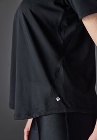 Tricou sport negru, confecționat dintr-o țesătură netedă, având mâneci scurte, croi lejer și un mic logo alb la tiv.