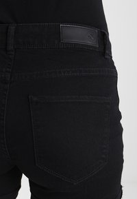 Černé džíny z denimu s texturovaným povrchem, pětikapsovým designem a černou koženou nášivkou na pasu.