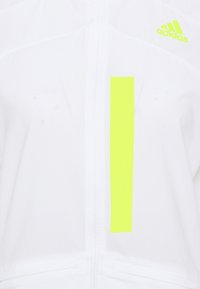 Giacca sportiva bianca con zip completa, caratterizzata da una striscia verticale gialla neon e dal logo Adidas in coordinato neon sul lato sinistro superiore.