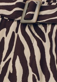 Ceinture avec boucle rectangulaire beige sur tissu à motif zèbre marron foncé et crème.