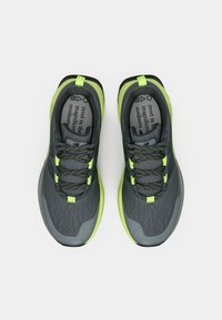 Δύο αθλητικά παπούτσια σε γκρι δίχτυ με φωτεινές πράσινες λεπτομέρειες. Διαθέτουν υφές στην επιφάνεια, αντανακλαστικά κορδόνια και ταινία τράβηγματος στη φτέρνα.