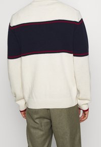 Gehaakte trui in crème met marineblauwe en rode horizontale strepen. Ronde halslijn en lange mouwen. Ribgebreide manchetten en zoom. Geweven stof.