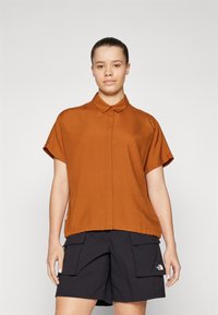 Short-sleeve collared shirt in burnt orange, featuring a button front and a relaxed fit, paired with black cargo shorts.
