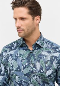 Kraagshirt met een marineblauwe basis en ingewikkelde paisleypatronen in groene en zilveren tinten. Gemaakt van zachte, gladde stof met knopen.
