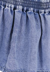 Denimrok in een lichtblauwe kleur, met een badstof tailleband en geplooide ruches langs de zoom voor extra textuur.