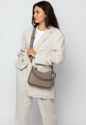 Beige leather handbag with a curved silhouette, gold hardware, and a detachable strap. Worn crossbody with textured surface details.