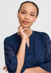 Bluză bleumarin cu broderie în formă de valuri, din material semi-transparent, cu decolteu în V și mâneci trei sferturi. Detaliile texturate îmbunătățesc designul.