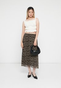 Weißes, gerafftes Crop-Top kombiniert mit einem fließenden, schwarzen Rock mit floralem Muster. Das Model hält eine schwarze, gebogene Handtasche und trägt schwarze High Heels.