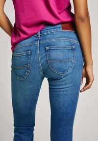 Kitsad sinised teksad pleekinud pesu, tugevdusõmblused ja kaks tagataskut. Kombineeritud roosa lühikeste varrukatega särgiga.