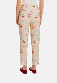 Beżowe spodnie z kolorowymi nadrukami, w tym wiśnie, serduszka i kwiatowe wzory. Materiał ma gładką teksturę, z prostym krojem nogawki.