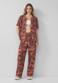 Losse, korteklassige blouse en wijde broek in roestkleur met een donker abstract patroon. Soepele stof, knoopsluiting op de blouse, casual ontwerp.