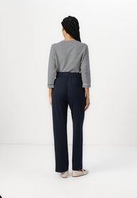 Camisa de manga larga a rayas en azul marino y blanco, combinada con pantalones de talle alto azul marino con bolsillos laterales. Unos zapatos en color crema completan el look.