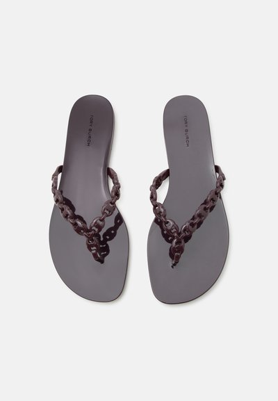 Γυαλιστερές σκοτεινές μοβ επίπεδες σαγιονάρες με συνδεδεμένους ιμάντες αλυσίδας και τυπωμένο το όνομα της μάρκας στη σόλα, τοποθετημένες δίπλα-δίπλα.