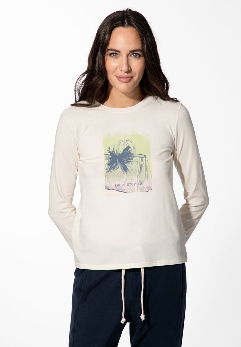 Crèmekleurig shirt met lange mouwen, voorzien van een grafische print van een handtas met een strik en de tekst "SHORT STORIES" in een gelaagde pastelkleurencombinatie.