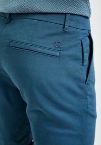 Shorts in cotone blu con una consistenza liscia, tasche frontali e una tasca posteriore con un'etichetta decorativa.