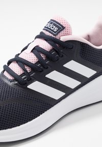 Svart och rosa Adidas löparskor med vita ränder, svarta snörningar och en dämpad sula på en vit bakgrund.