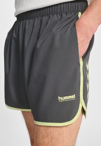 Grå idrottsshorts i lätt material, med limegröna detaljer, elastisk midja och sidofickor. "hummel"-logotypen visas.