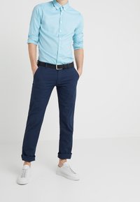 Jasnoniebieska koszula zapinana na guziki, granatowe spodnie, czarny pasek oraz białe trampki. Swobodny krój z podwiniętymi rękawami i gładką fakturą.