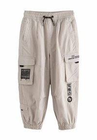 Beige Cargo-Hosen mit elastischem Taillenbund, Kordelzug, Seitentaschen und zwei Cargo-Taschen mit schwarzen grafischen Designs und gestreiften Akzenten.