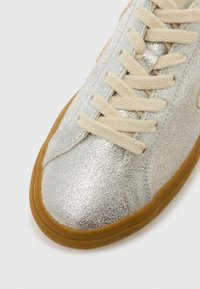 Ασημί μεταλλικό αθλητικό παπούτσι με υφή, με κορδόνια σε κρεμ απόχρωση, λαστιχένια σόλα και απλό σχέδιο χωρίς επιπλέον μοτίβα.